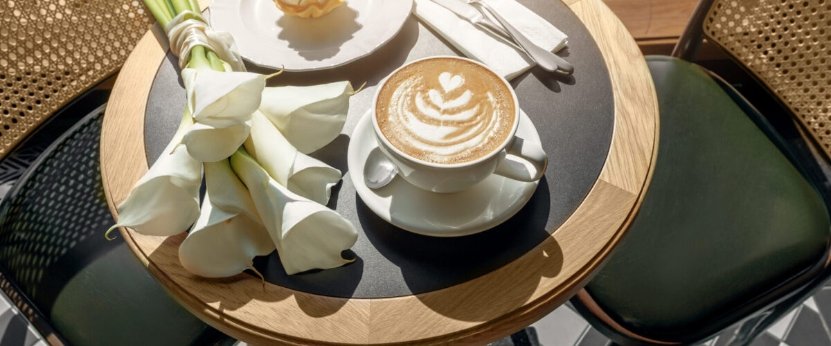 Cappuccino, delicious whipped creme dessert and white calla flowers on wooden table in cafe. Mockup for cafe or restaurant. Love and romance concept.